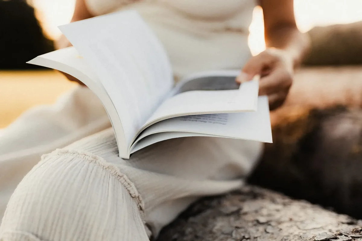 Ein aufgeschlagenes Buch liegt auf dem Schoß, eine Hand blättert eine Seite um