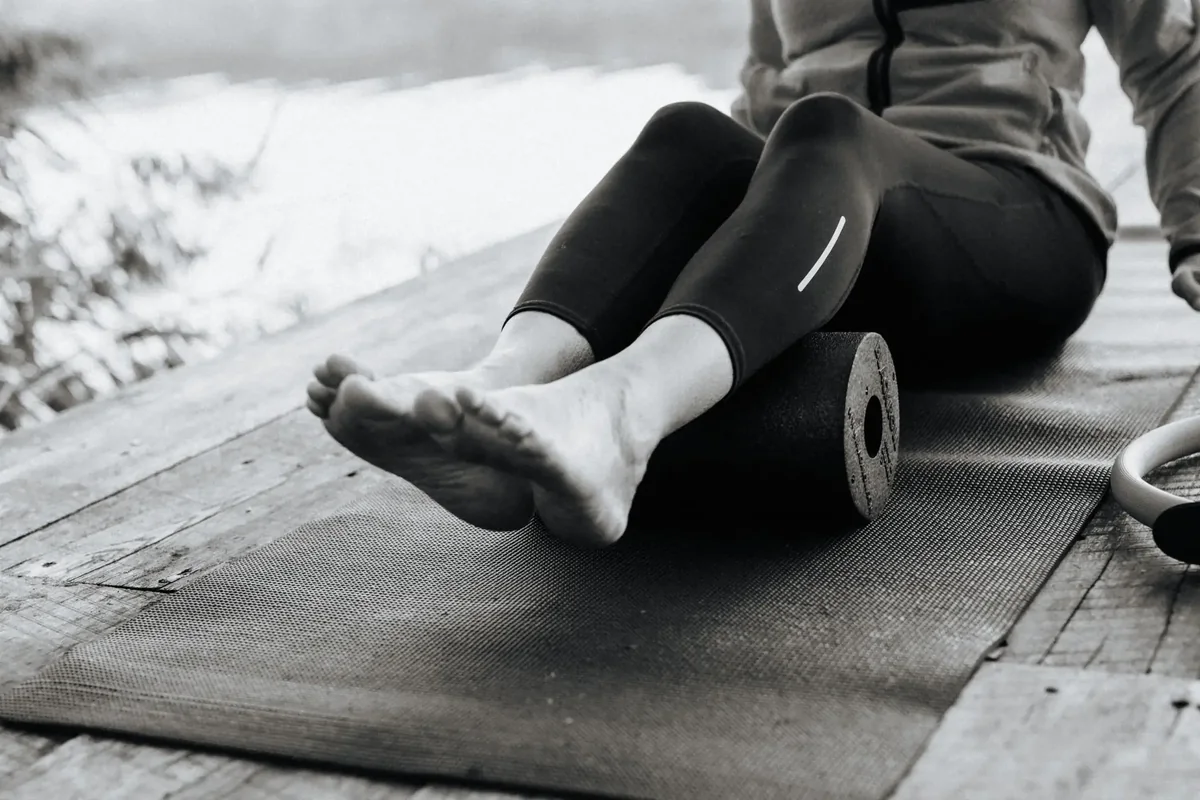 Schwarzweißaufnahme: Füße und Beine liegen auf einer Faszienrolle auf der Pilates-Matte