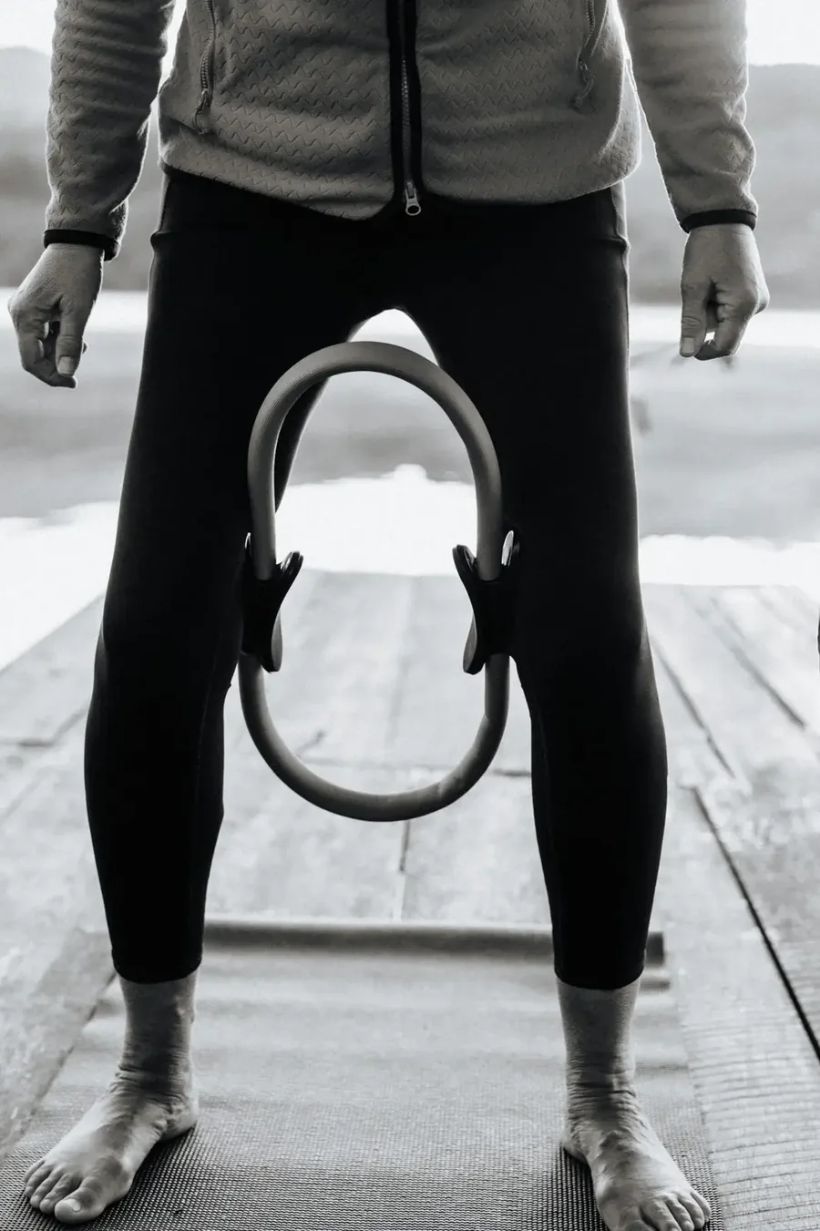 Schwarzweißaufnahme: Beine mit einem Pilates-Ring zwischen den Knien auf einer Matte