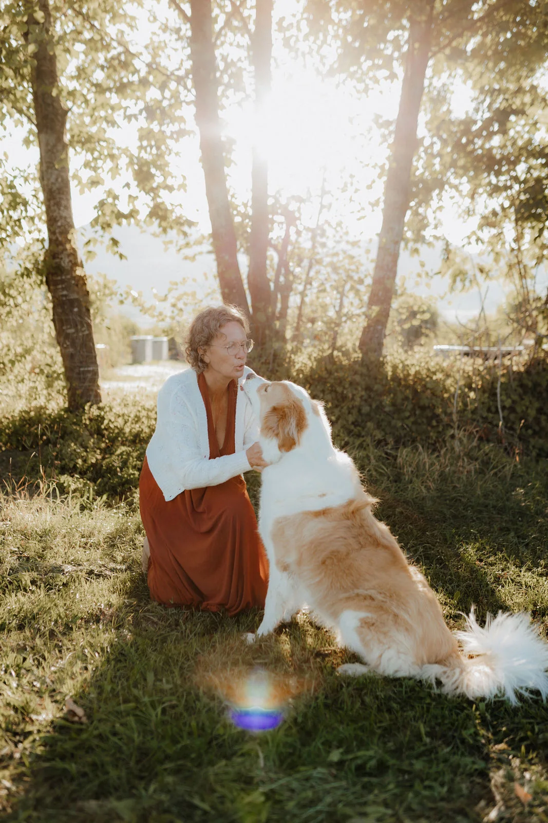 Renate Troppmair kniet im Abendlicht unter Bäumen, ihr Hund Semmy schaut sie an