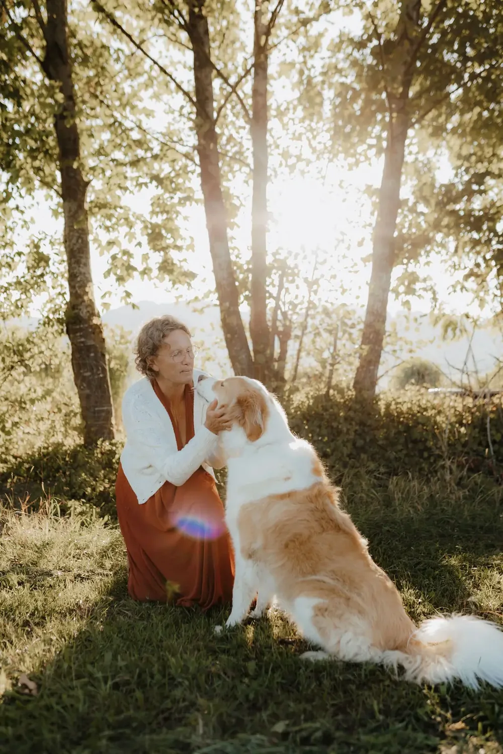 Renate Troppmair streichelt ihren Hund Semmy unter Bäumen im Gegenlicht